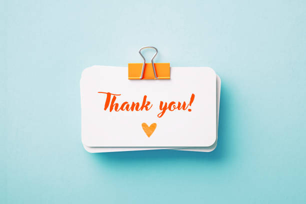 Thank you note held by an orange paper clip on blue background. Horizontal composition with copy space. Reminder concept.