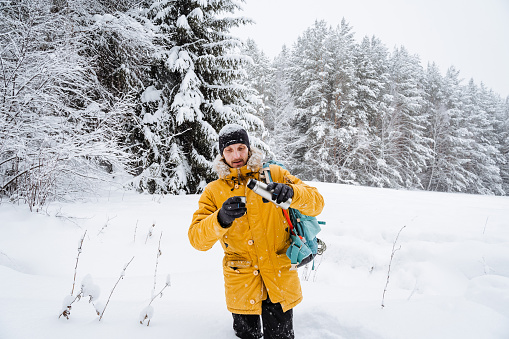 El viajero sonriente y feliz bebe té o café caliente en termos. Bosque nevado y rocas. Subir a la montaña en invierno. Supervivencia en la naturaleza. photo