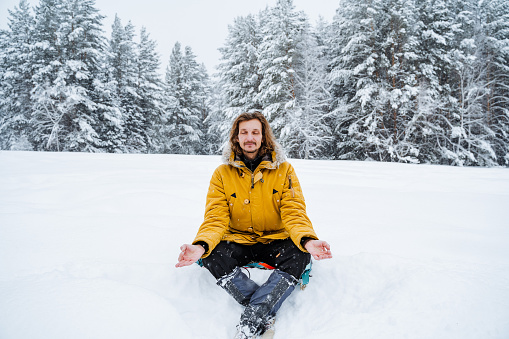 A happy man rejoices in the snowfall. A man sits in the snow. Panoramic view of the forest. A walk in the forest in winter. Meditation.High quality photo