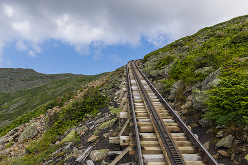 Steep and bending part of the Mt Washington cog railway track disappearing behind a mountain, New Hampshire, USA