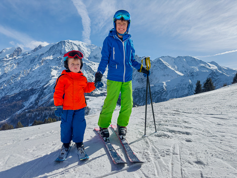Big brother skier bond with little sibling teaching him to ride on sunny slope in French mountains