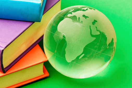 A glass globe-shaped paperweight on a green background next to a pile of books. Seems someone is studying the world. 