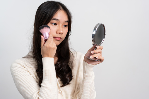 Beautiful young woman makes blush on her face using makeup brush on isolated white background. Teenage girl doing her own makeup. Close up portrait. Copy, empty space for text