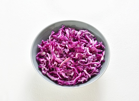 Red cabbage in bowl on white stone background. Close up view