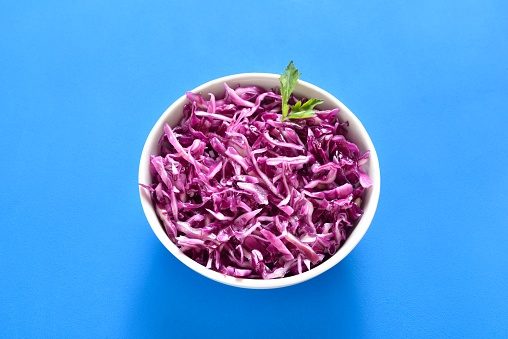 Red cabbage in bowl on blue background. Close up view