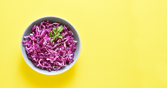Red cabbage in bowl over yellow background with copy space. Top view, flat lay