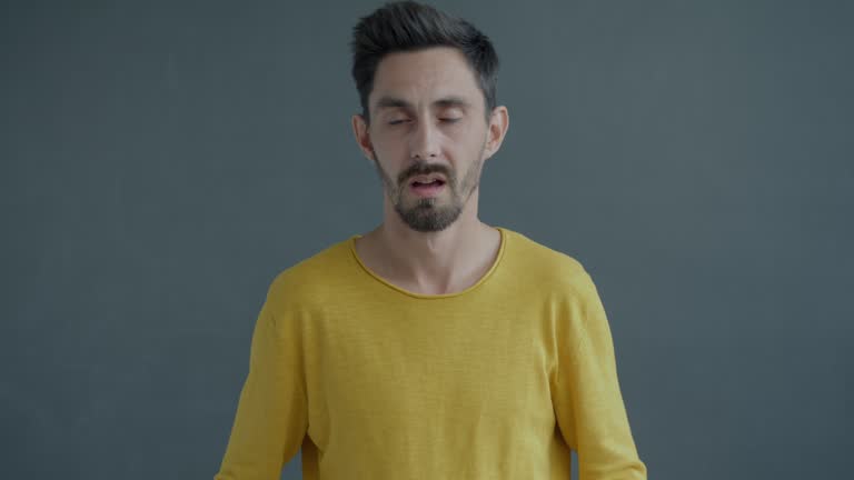 Slow motion portrait of annoyed guy looking at camera expressing disappointment and discontent on grey background