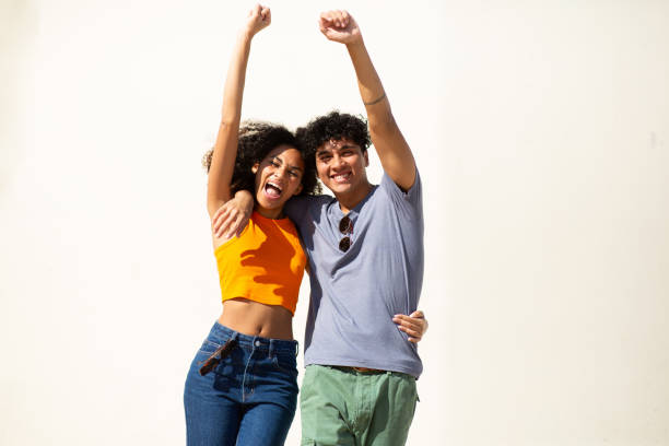 istock cheerful young couple with arms raised by white background 1759736645