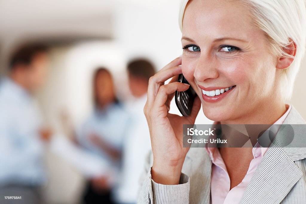 Smiling young lady using mobile phone at office  Business Stock Photo