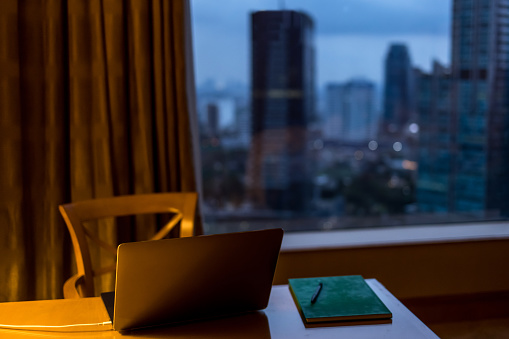 Laptop on the desktop in modern studio or office against nighttime cityscape window background