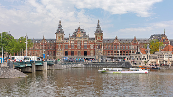 Amsterdam, Netherlands - May 16, 2018: Main Train Station Building in City Centre View Over Water Canal Spring Day.