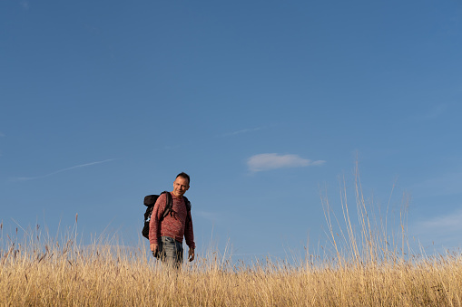 Young man hiking through autumn fields and hills against blue sky during warm day. Weekend, leisure, sport concept