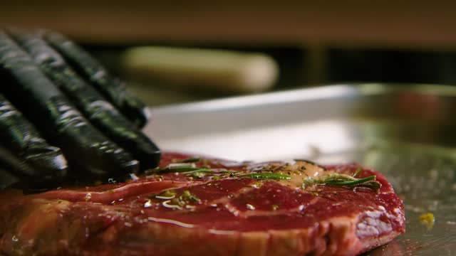 Chef squirts and rubs olive oil into beautiful cut of steak with herbs on metal tray