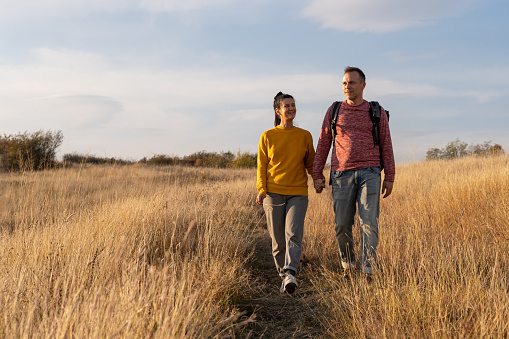 Young couple hiking through autumn fields and hills during warm day. Weekend, leisure, sport concept