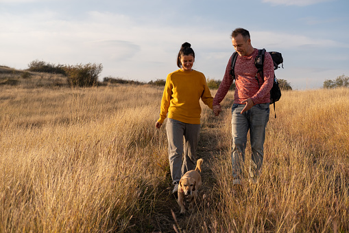 Young couple hiking through autumn fields and hills during warm day with their dog. Weekend, leisure, sport concept