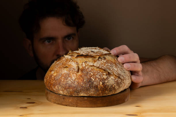 istock Attractive young Caucasian chef posing with white sourdough bread. The sourdough bread is the central protagonist of the scene, standing out with beautiful golden tones against the dark background. 1759800682