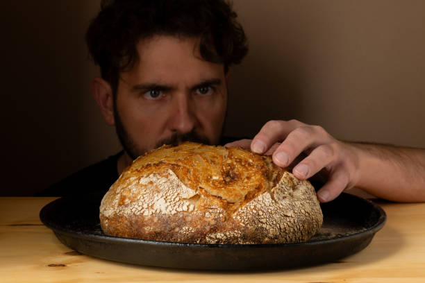 istock Attractive young Caucasian chef posing with white sourdough bread. The sourdough bread is the central protagonist of the scene, standing out with beautiful golden tones against the dark background. 1759800683