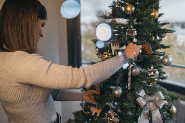 istock Young woman placing a string of decorative lights on Christmas tree. 1759801238