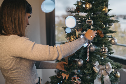 Young woman placing a string of decorative lights on Christmas tree.
