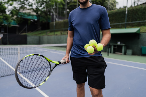 Midsection of a man holding a racket and tennis balls