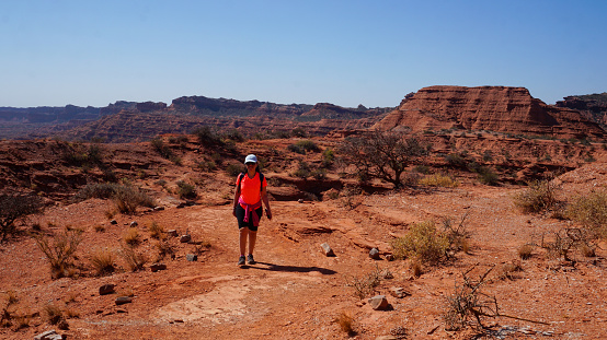 young woman hiking  in a dirt path near a few small hills in \