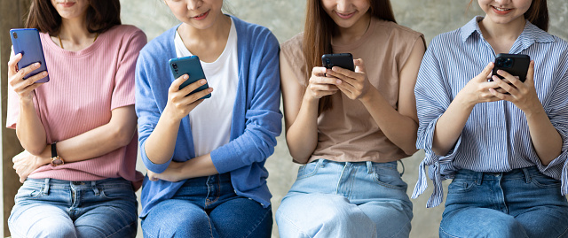 Group of young women using mobile phone. Young people sitting together obsessed with devices online, asian using laptops and smartphones, digital life and gadgets overuse concept.