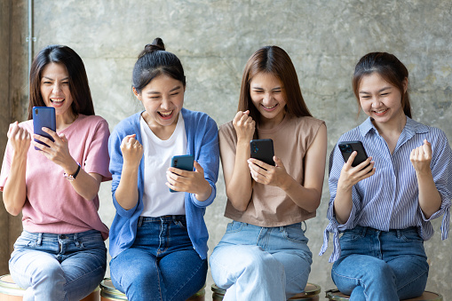 Group of young women using mobile phone. Young people sitting together obsessed with devices online, asian using laptops and smartphones, digital life and gadgets overuse concept.