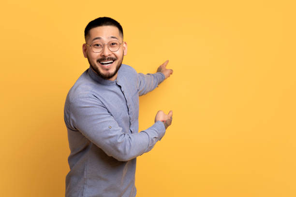 istock Cheerful Excited Asian Man Pointing At Copy Space On Yellow Background 1759879476