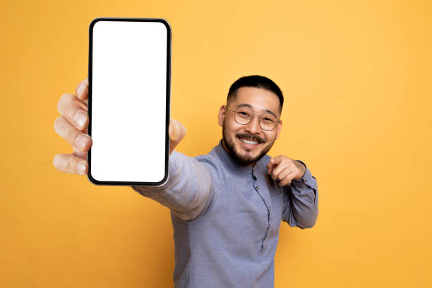 istock Mobile Advertisement. Cheerful Asian Man Pointing At Big Blank Smartphone In Hand 1759879767