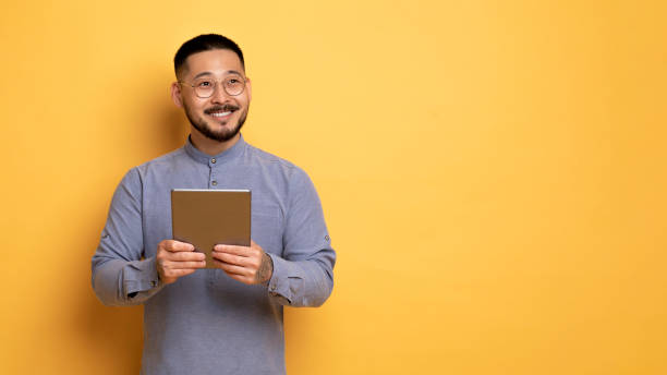 istock Young Smiling Asian Man Holding Digital Tablet And Looking Away 1759880009