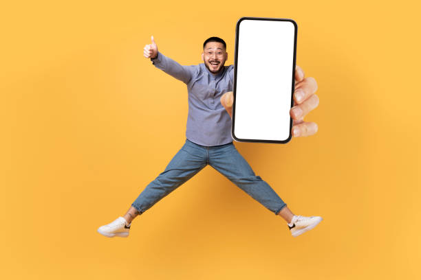 istock Great Offer. Asian Man Jumping With Blank Smartphone And Gesturing Thumb Up 1759880018