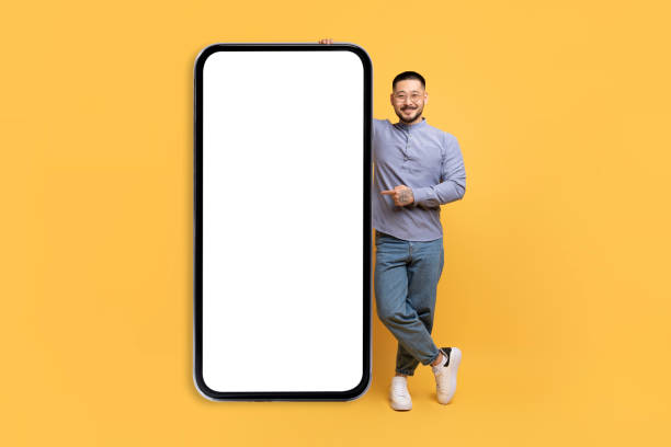 istock Young Asian Man Leaning And Pointing At Big Smartphone With Blank Screen 1759880026