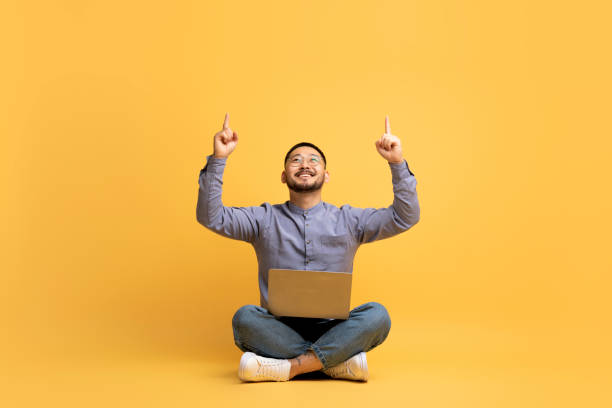 istock Check This. Smiling Asian Man With Laptop Pointing Up At Copy Space 1759880032