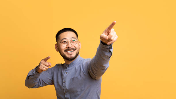 istock Gotcha. Cheerful asian man pointing away with two hands 1759880042