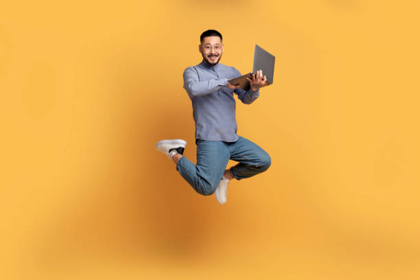 istock Happy asian man with laptop computer jumping up over yellow background 1759880669