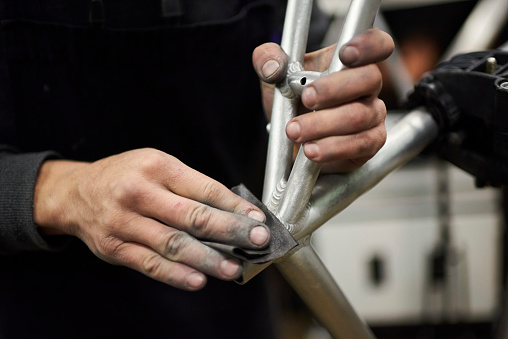 Hands of an unrecognizable hispanic man sanding an unpainted bicycle frame as part of the process of a bike renovation work made at his workshop.