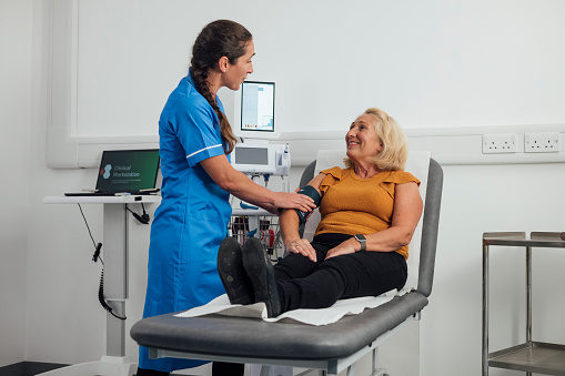 A medium wide angle view of a mature woman who is getting a health checkup and getting her blood pressure and heart health checked by a medical professional in a clinic in Newcastle Upon Tyne in the North East of England.