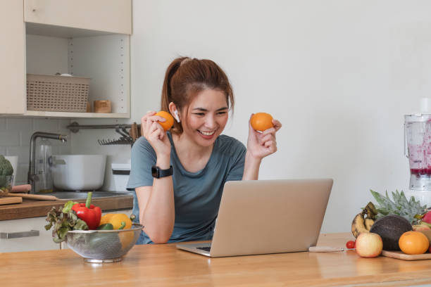 istock Beautiful young woman in exercise clothes having fun in a cute kitchen at home. Using your laptop to prepare vegan fruit salad dressing, fruit shakes, or healthy smoothies. 1759900198