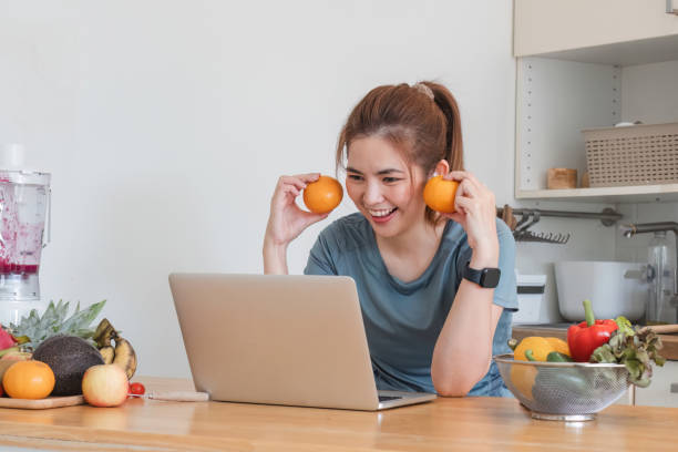 istock Beautiful young woman in exercise clothes having fun in a cute kitchen at home. Using your laptop to prepare vegan fruit salad dressing, fruit shakes, or healthy smoothies. 1759900202