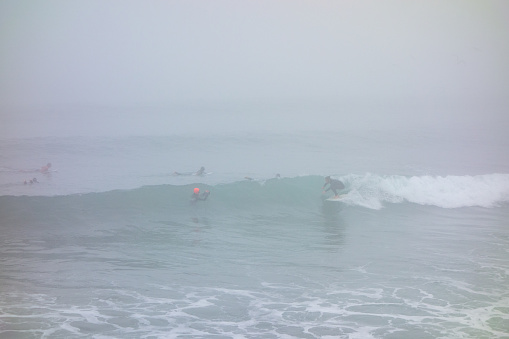 Surfers surfing on a cloudy morning right of the Venice fishing pier in Venice Beach, California.