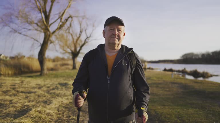 Senior man with trekking poles in their hands on the lake, Nordic walking, enjoy nature at sunset time.