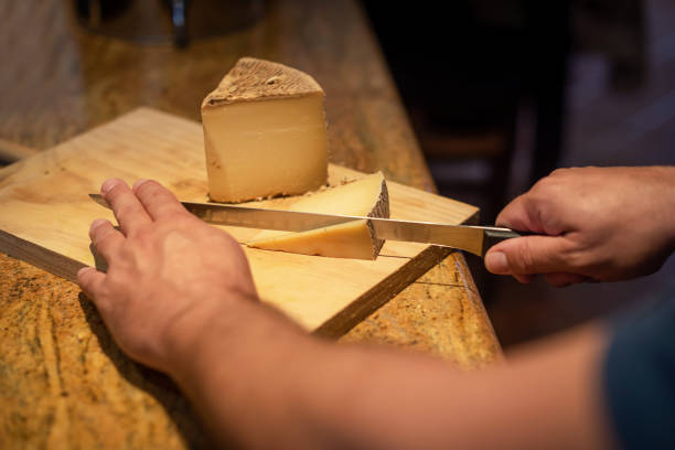 istock Selective focus on a man slicing cheese wedges on a wooden board with a long knife. Tasting aged cheese 1759950680