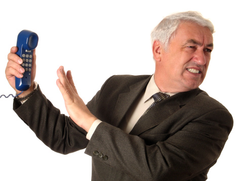 A man in a suit averting his face discontentedly from the phone receiver in his hand (isolated on white)