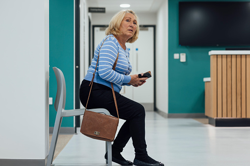 A medium side view of a mature home who is sitting in a doctors waiting room in a doctors surgery in Newcastle upon tyne in the North East of England.