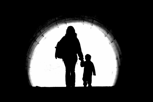 A mother holds the hand of her son, walking through a tunnel.