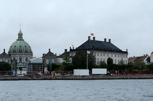 Copenhagen, Denmark – October 06, 2023: A tranquil body of water with a picturesque shoreline of lush greenery and architectural buildings in the background