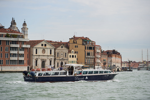 Tourist cruise boat in Venetian canal. Modern tour boat cruising the Guidecca canal in spring. Venice - 5 May, 2019