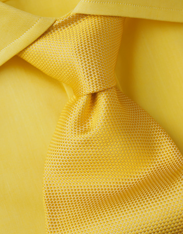 A yellow shirt with a yellow tie in close-up.