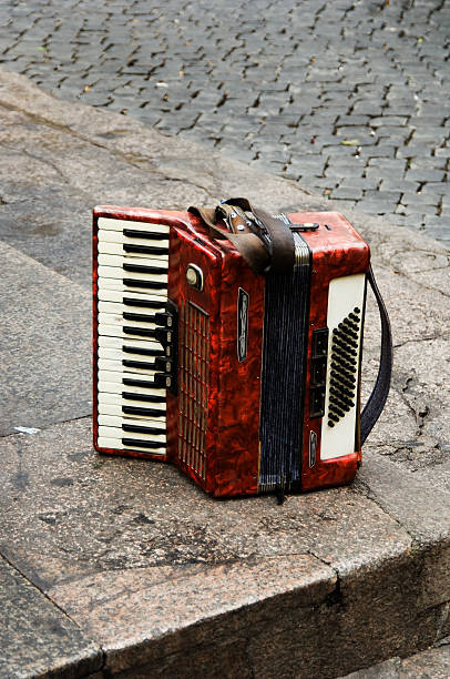 The mature caucasian man dressed in a military jacket with St. George ribbon on his chest. The man is sitting and playing an accordion a folk music. He smiling looking aside. Studio shooting