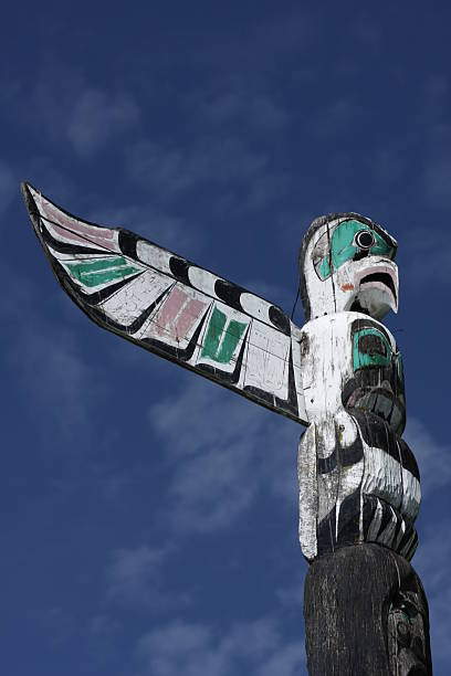 Totem Pole and Blue Sky in British Columbia, Canada, Summer "A totem pole in Vancouver, British Columbia, Canada. Carving of a bird with outstretched, multi-coloured wing." pacific northwest totem poles stock pictures, royalty-free photos & images